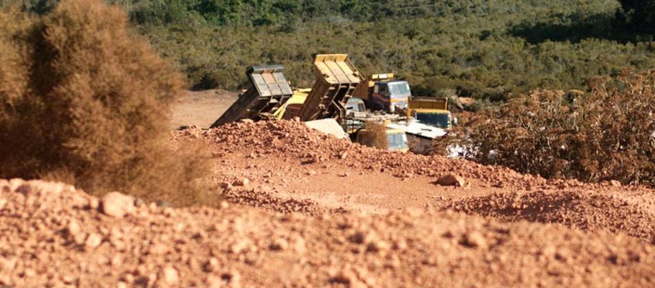 Terre rouge au premier plan séparée des forêts en contrebas par des camions chargeant de la bauxite