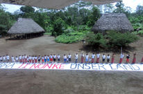 Vue aérienne. Des amérindiens d'Amazonie équatoriale ont déployé devant eux sur le sol une immense banderole sur laquelle est inscrit le message « C'est notre terre »