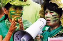 Gros plan sur deux femmes maquillées de bleu et de vert lors d'une manifestation. L'une tape dans les mains, l'autre parle dans un mégaphone