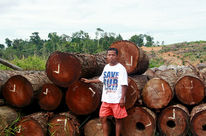 Notre partenaire Nordin de l'organisation Save our Borneo pose devant un tas de troncs d'arbres tropicaux