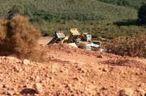 Terre rouge au premier plan séparée des forêts en contrebas par des camions chargeant de la bauxite