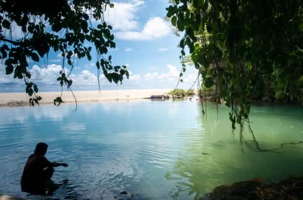 Une femme est assise dans l’eau dans une baie bordée de sable et de rochers