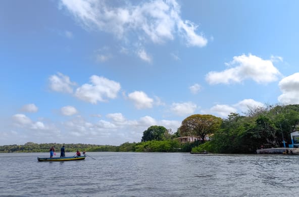 Trois personnes dans une petite barque au milieu d’un cours d’eau aux rives boisées