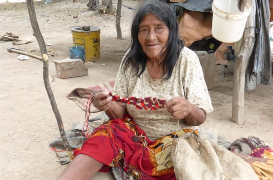 Une indigène Manjui assise sur le sol travaille un tissu en fibres végétales