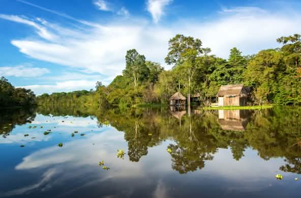 La forêt amazonienne et une cabane en bois se reflètent dans l’eau du fleuve Yanayacu au Pérou
