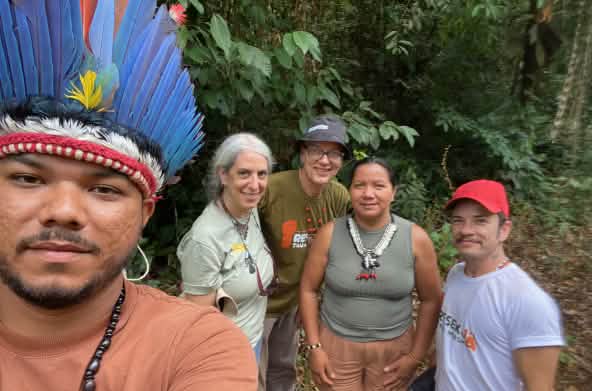 Un indigène avec une coiffe à plumes (à gauche) fait un selfie avec quatre personnes derrière lui dans la forêt tropicale
