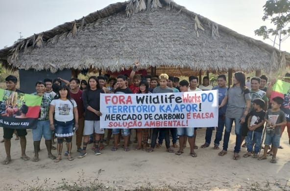 30 indigènes manifestent devant une hutte : « Wildlife Works, sortez du territoire des Ka’apor. Le commerce du carbone n’est pas une solution environnementale viable »