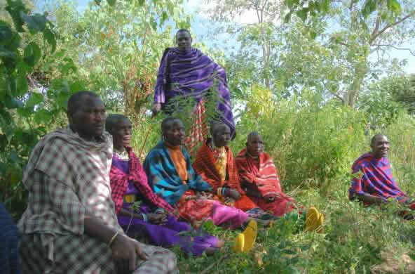 Un groupe d’hommes Masaï est assis dans l’herbe, vêtus de couvertures colorées