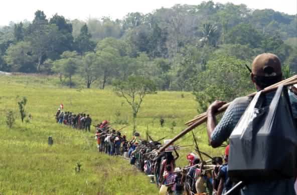 File indienne d’indigènes qui traversent une savane en allant à la chasse,