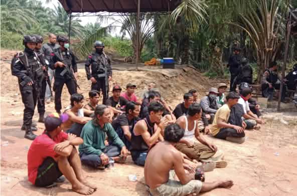 Des autochtones du peuple Dayak sont assis par terre, avec des policiers lourdements armés derrière eux