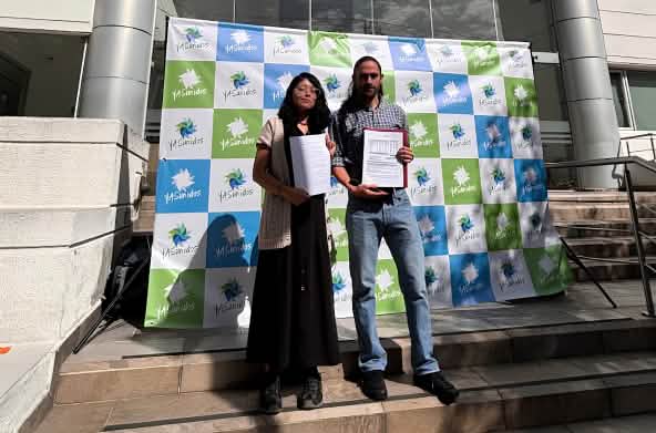 Une femme et un homme se tenant devant l’entrée d’un immeuble, à côté d’une banderole sur laquelle on peut lire « YASunidos », tenant des documents à la main