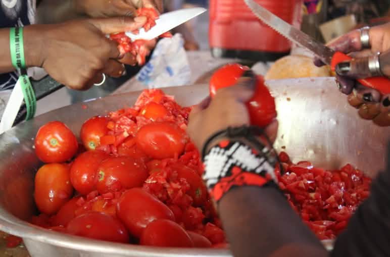 Gros plan sur les mains de deux personnes en train de couper des tomates sur un saladier en métal