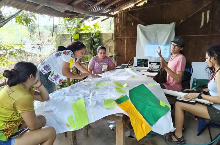 Cinq femmes assises autour d’une table travaillent sur des supports
