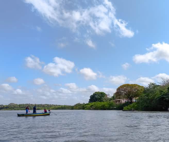 Trois personnes dans une petite barque au milieu d’un cours d’eau aux rives boisées
