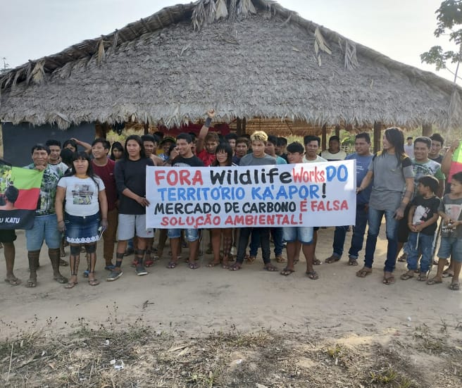 30 indigènes manifestent devant une hutte : « Wildlife Works, sortez du territoire des Ka’apor. Le commerce du carbone n’est pas une solution environnementale viable »