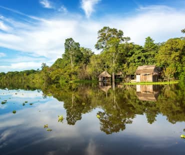La forêt amazonienne et une cabane en bois se reflètent dans l’eau du fleuve Yanayacu au Pérou
