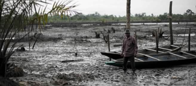 Un homme se tient debout dans le lit d’une rivière polluée par le pétrole dans le delta du Niger