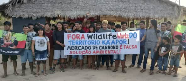 Les autochtones Ka’apor protestent contre la marchandisation illégale de leur forêt tropicale (© TUXA TA PAME) 30 indigènes manifestent devant une hutte : « Wildlife Works, sortez du territoire des Ka’apor. Le commerce du carbone n’est pas une solution environnementale viable »