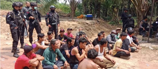 Des autochtones du peuple Dayak sont assis par terre, avec des policiers lourdements armés derrière eux