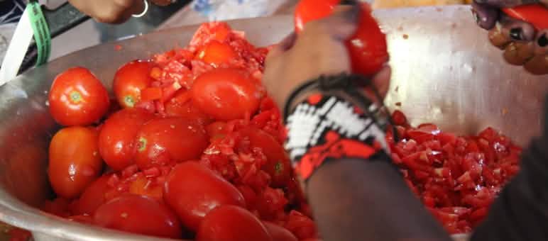 Gros plan sur les mains de deux personnes en train de couper des tomates sur un saladier en métal
