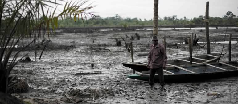 L’extraction d’énergies fossiles détruit les moyens de subsistance des populations locales Un homme se tient debout dans le lit d’une rivière polluée par le pétrole dans le delta du Niger
