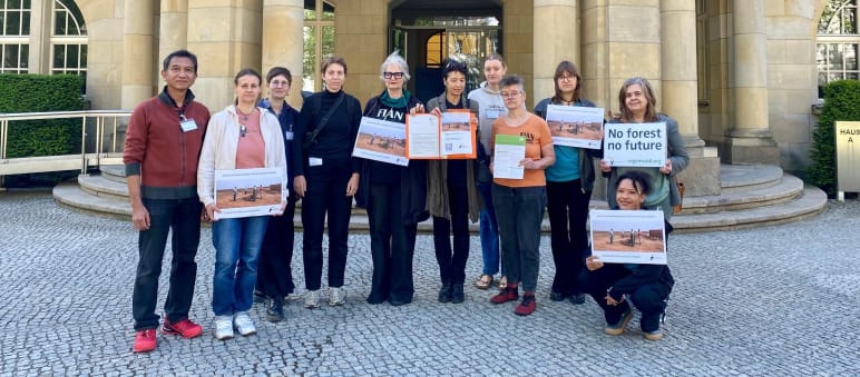 Des personnes représentant les organisations Rettet den Regenwald (Sauvons la forêt), FIAN, Powershift et Weed posent avec des pancartes devant le perron d’un bâtiment ancien
