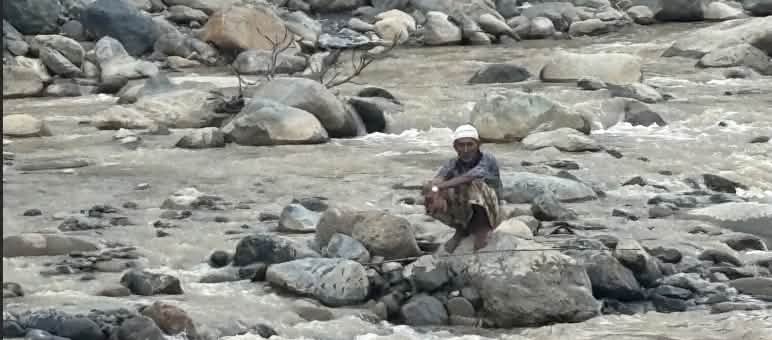 Un homme assis sur un rocher dans la rivière