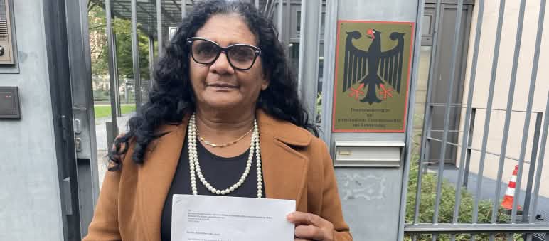 La femme quilombola Marli Borges tenant une lettre devant l’entrée grillagée du Ministère fédéral de la Coopération économique et du Développement (BMZ)