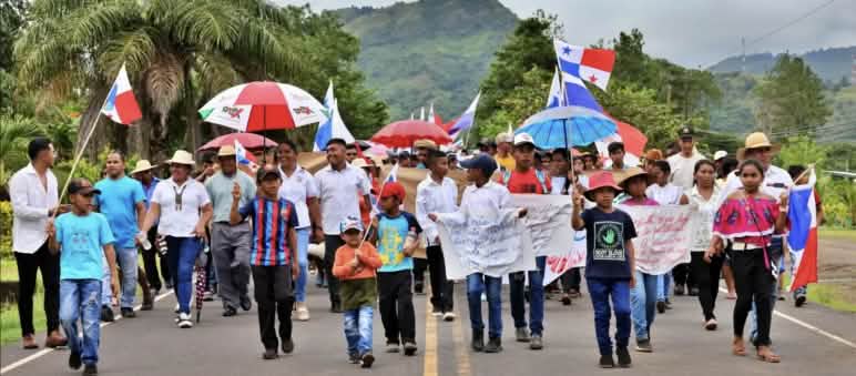 Des personnes défilent sur une route de campagne au Panama avec des bannières, des drapeaux du Panama et des parapluies assortis