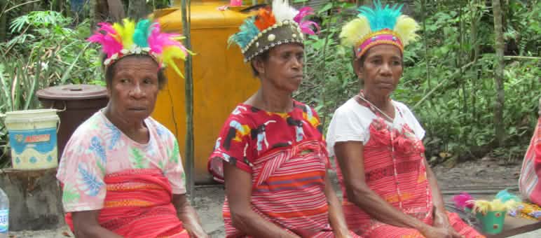 Trois femmes vêtues de tissus rouges et coiffées de plumes colorées