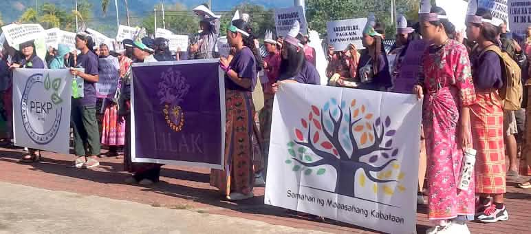 Un rassemblement de femmes et de jeunes en tenue traditionnelle brandissant des pancartes colorées pour protester contre l’exploitation minière