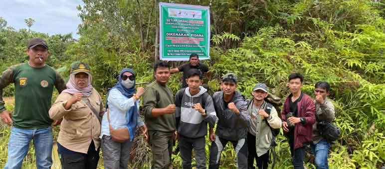 Un groupe de personnes devant un panneau indiquant que toute activité dans la forêt est passible de lourdes amendes
