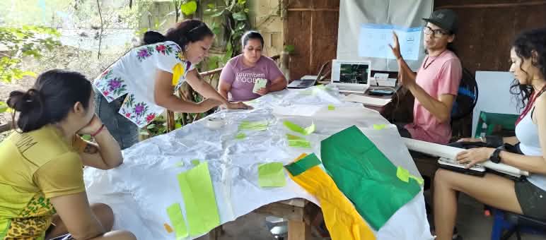 Cinq femmes assises autour d’une table travaillent sur des supports