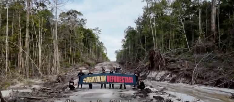 Des activistes protestent au milieu d’une route de bûcheronnage. Ils brandissent une bannière sur laquelle est écrit « Halte à la déforestation ! » en indonésien.