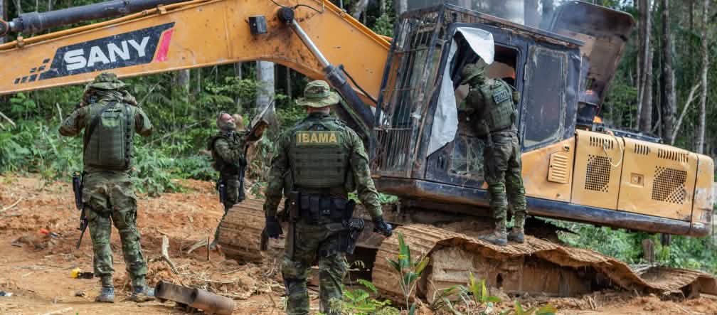 Des agents de l’agence environnementale IBAMA détruisent une excavatrice utilisée pour l’exploitation illégale de l’or dans la forêt des indigènes Munduruku Quatre hommes armés en tenue de camouflage détruisent une pelleteuse jaune au milieu de la forêt tropicale
