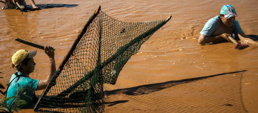 Trois hommes pêchent dans les eaux brunes d’un lac