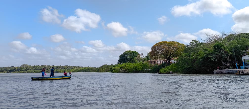 Trois personnes dans une petite barque au milieu d’un cours d’eau aux rives boisées