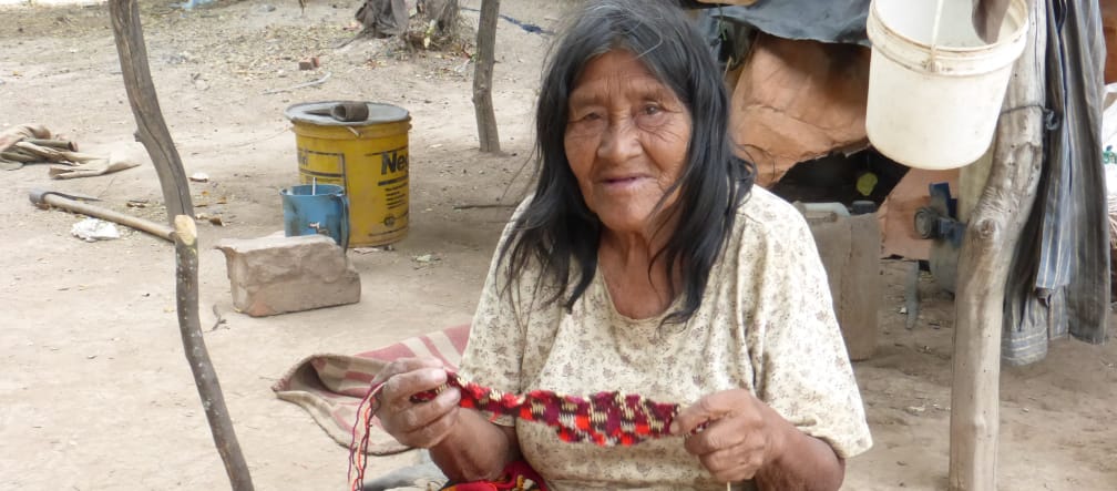 Une indigène Manjui assise sur le sol travaille un tissu en fibres végétales