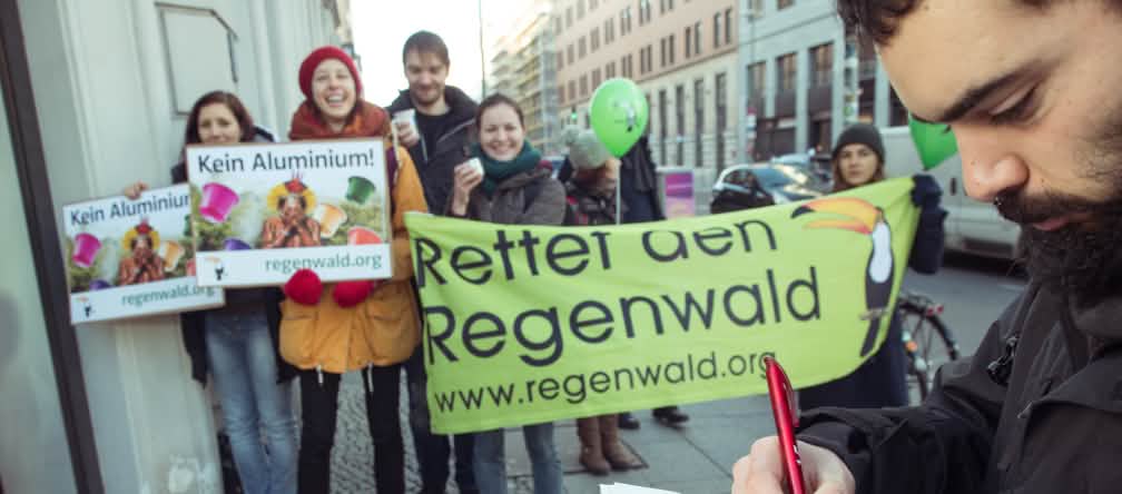 Au premier plan un homme signe une pétition de Sauvons la forêt. En arrière plan des activistes avec leurs banderoles et pancartes devant une boutique Nespresso à Berlin.
