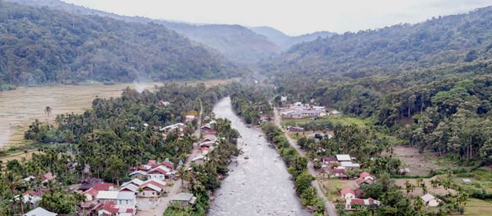 Vue aérienne d’une rivière traversant un village, avec des montagnes en arrière-plan