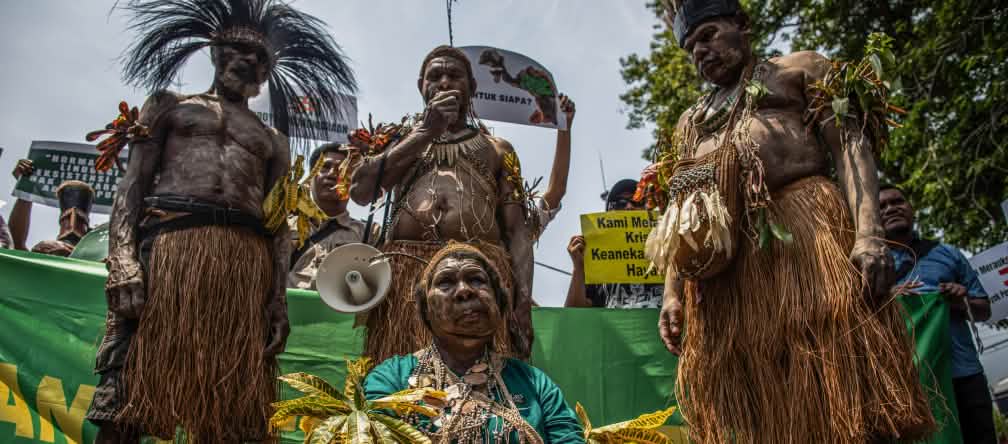 Quatre autochtones papous en tenue traditionnelle devant des bannières lors d’une manifestation à Jakarta