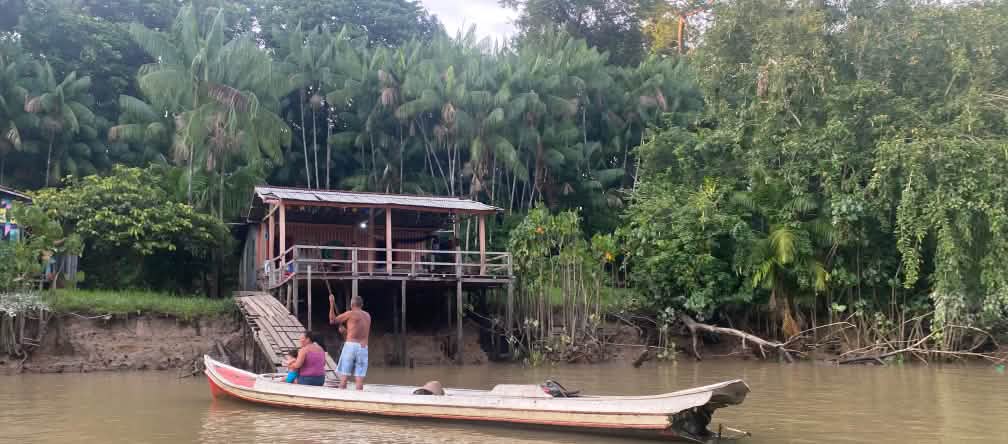 Deux personnes dans un bateau en bois devant une cabane en bois au bord d’une rivière dans la forêt tropicale