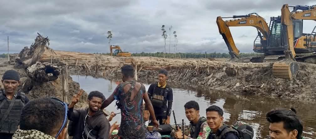 Groupe d’hommes avec, en arrière plan, des pelles mécaniques devant un paysage dévasté
