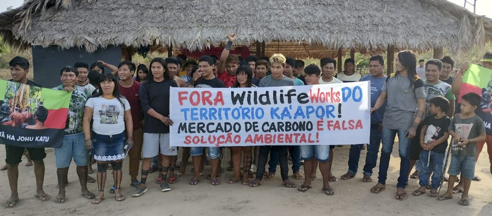 Les autochtones Ka’apor protestent contre la marchandisation illégale de leur forêt tropicale 30 indigènes manifestent devant une hutte : « Wildlife Works, sortez du territoire des Ka’apor. Le commerce du carbone n’est pas une solution environnementale viable »