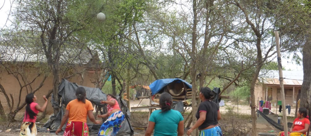 Cinq femmes amérindiennes jouent au ballon entre les arbres et les maisons en bois