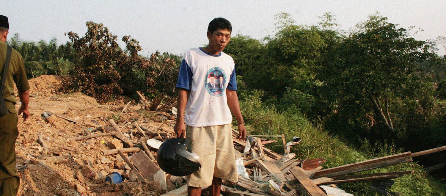 Un paysan se tient devant son village en ruines