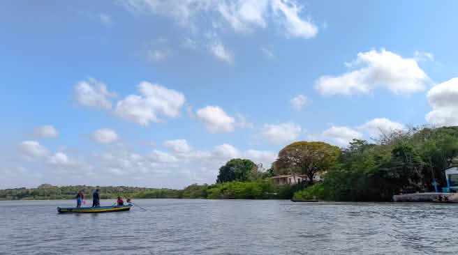 Trois personnes dans une petite barque au milieu d’un cours d’eau aux rives boisées