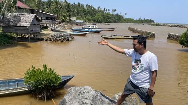 Amien Muhammad (Alliansi Sulawesi) montre l’eau polluée visible derrière lui, le long d’une côte tropicale.