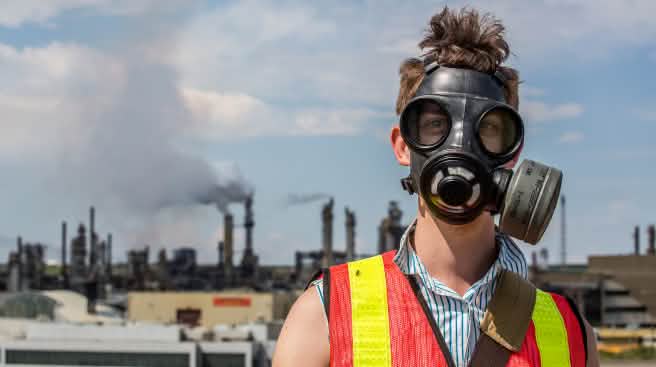 Le pétrole issu des sables bitumineux est le plus nocif au monde pour le climat Un jeune homme portant à masque à gaz avec en arrière plan une usine de traitement de sables bitumneux au Canada