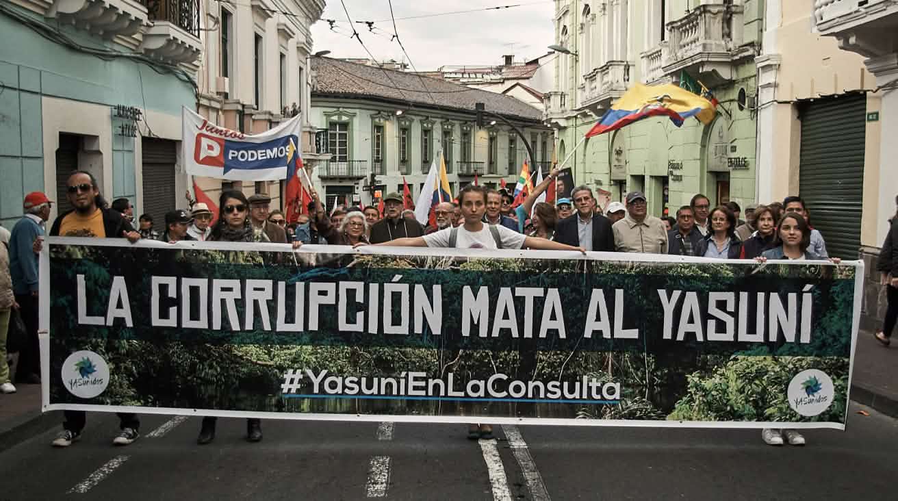 Un cortège défile dans une rue avec une grande banderole portant le slogan, en espagnol, « La corruption tue le Yasuní »